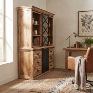 Een gedetailleerde foto van de buffetkast mangohout 160cm, waarbij de nadruk ligt op de textuur en de metalen schuifdeur. De kast staat naast een bureau met een bureaulamp en een stapel boeken. Op de voorgrond is een deel van een leren bureaustoel en een vloerkleed zichtbaar. De algehele sfeer is warm en natuurlijk.