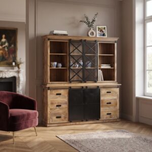 Een sfeervolle interieurfoto van de buffetkast mangohout 200cm in een warme woonkamer setting. De kast is gedecoreerd met servies, boeken en ingelijste foto's, met links een dieprode fauteuil en een klassieke schouw op de achtergrond.