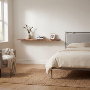 Een gezellige slaapkamer met een Zwevende wandplank Walnoot mangohout 180cm boven een bed, gestyled met een vaas eucalyptus, boeken en een fotolijst, naast een fauteuil met een deken.